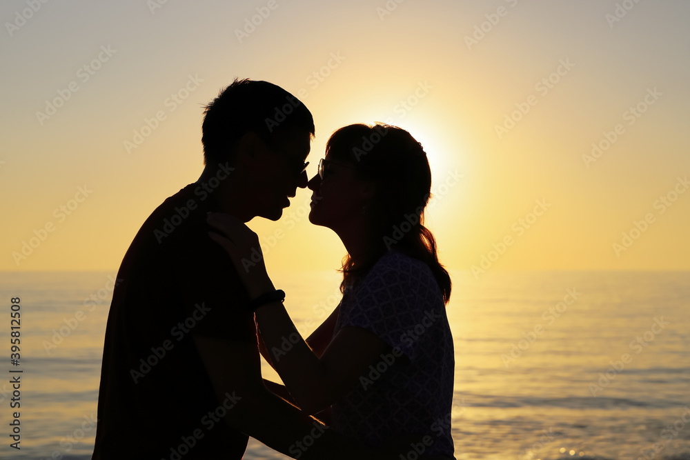 Silhouette of couple in love who touch each other with their noses against the backdrop of the setting sun. Happy relationship concept with copy space