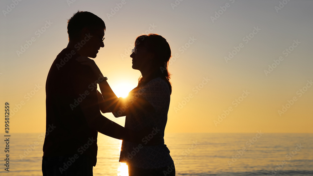 Young man and woman are in love, looking at each other closely. Silhouette at sunset with copy space