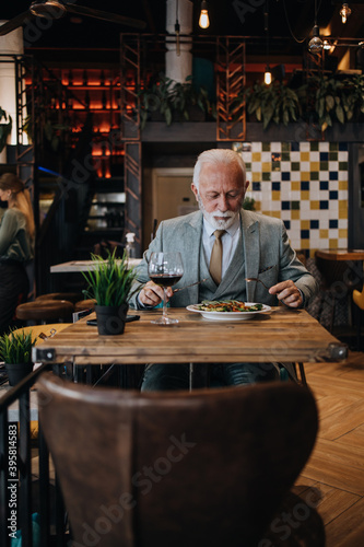 Happy businessman sitting in restaurant and having lunch. He is enjoying in delicious food and wine.