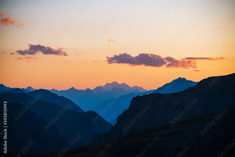 Fototapeta premium Colorful dawn landscape with beautiful mountains silhouettes and golden gradient sky with lilac clouds. Vivid mountain scenery with picturesque multicolor sunset. Scenic sunrise view to mountain range