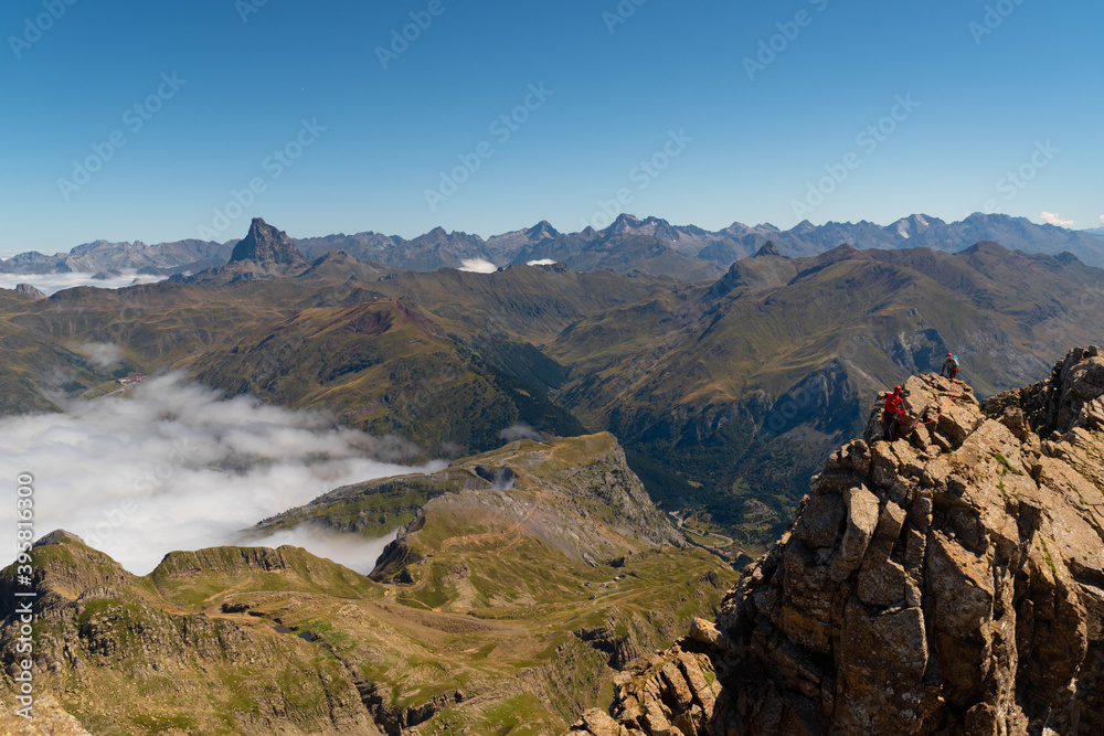 Two anonymous climbers reaching Aspe peak in the Pyrenees with peaks and mountains on the Spanish side and a sea of clouds on the French side