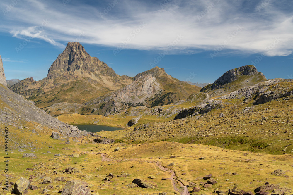Mountain path with a lake and the Midi d'Ossau peak in the background surrounded by mountains, rocks and nature