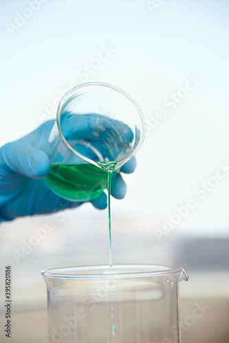 Gloved Hand Pouring Green Liquid Into Beaker
