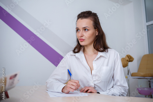 A beautiful young woman sits at a table and signs important documents.