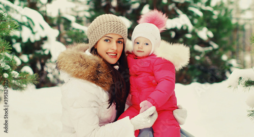 Portrait of happy smiling mother and little child in winter day together over snowy background
