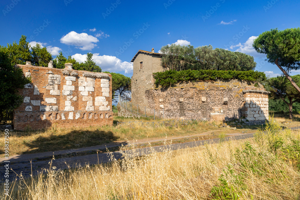 Fototapeta premium The imposing brick mausoleum, Casal Rotondo Mausoleum, Via Appia Antica Rome, photographed on a day with sun and clouds. Remains of the pavement, maritime pines, the Roman countryside.