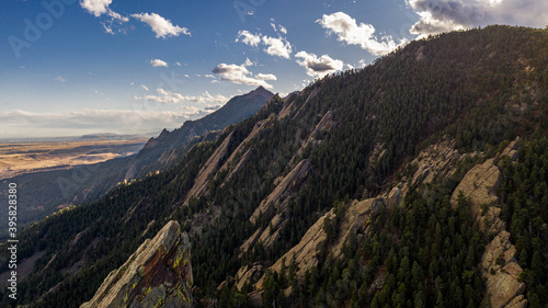 Drone view of the flatirons in Boulder Colorado. A mountain peak can be seen in the background as well as several rock formations in the forest.