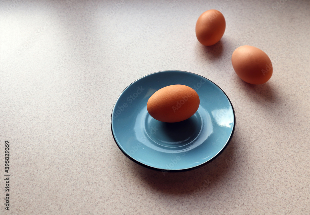 Chicken eggs on a blue plate and on a gray kitchen table with evening shadows, side view-the concept of using fresh eggs in cooking Chicken eggs on a blue plate and on a gray kitchen table with evening shadows, side view-the concept of using fresh eggs in cooking
