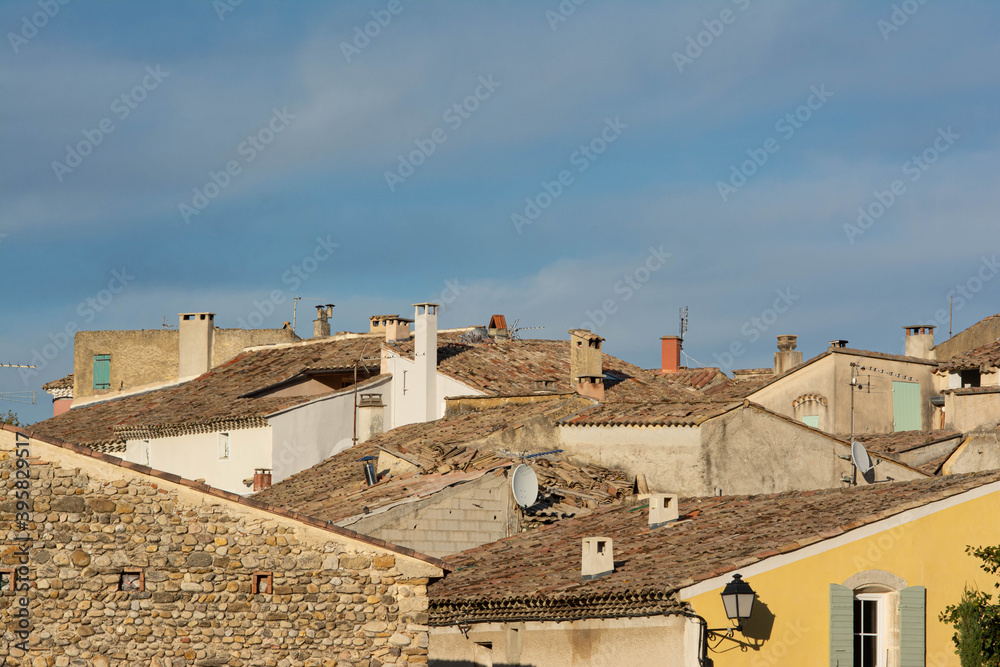 Roofs of a Provencal village, lanterns, windows, shutters, plaster. Pebble walls. Cloudy blue sky.