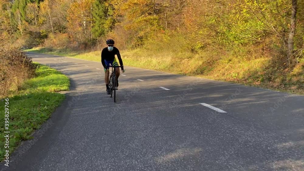 Cyclist cycling with mask up the road in the autumn colors sunny weather and blue sky during covid coronavirus Cyclist cycling with mask up the road in the autumn colors sunny weather and blue sky during covid coronavirus