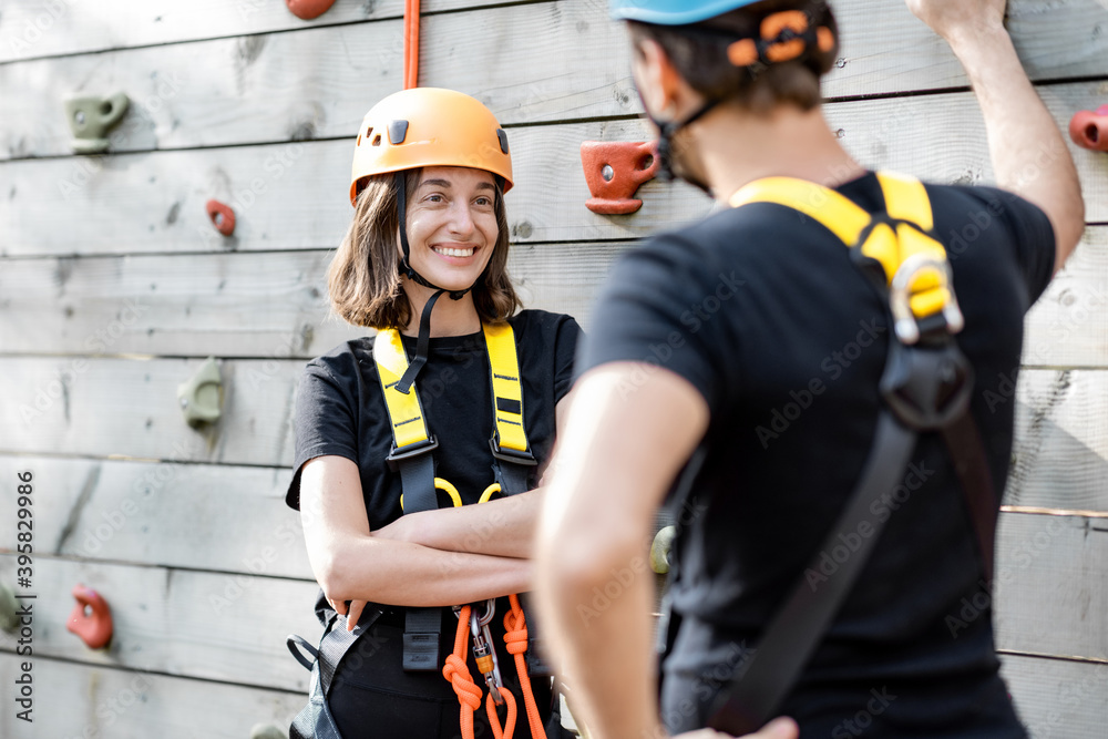 Obraz premium Sports well-equipped couple talking and having fun near the climbing wall, ready for the climbing at amusement park