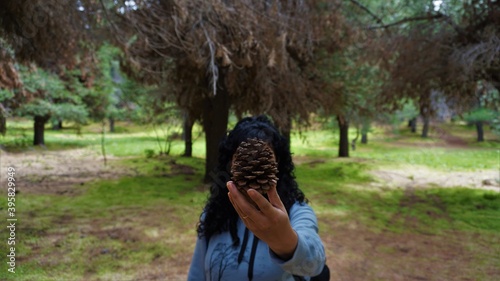 Mujer en el bosque rodeada de pinos mostrando una piña