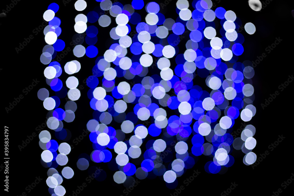 Fototapeta premium blue and white blurred spots from the garland on the black background. Blurred abstract white and blue spot lights isolated on dark background. new year and christmas bright background 