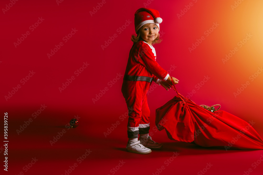 Little girl with a sack of Santa Claus on a red background with empty side space. Merry christmas and a happy new year.