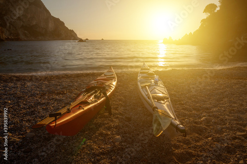 Fototapeta Naklejka Na Ścianę i Meble -  Two kayak (canoe) from paddles stand on the shore of a pebble beach. Beautiful warm sunny evening on the warm coast of the Adriatic Sea. Quiet water surface in an incredible closed bay.