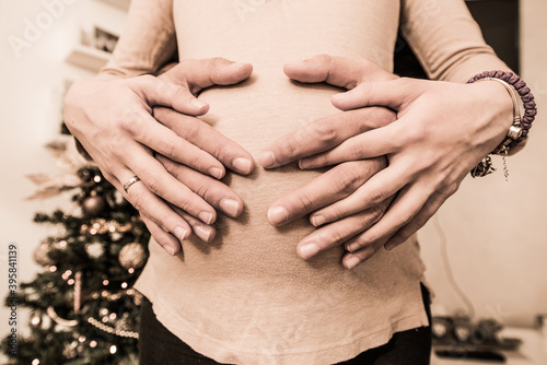 Hands on women belly of young future parents while expecting baby at new years. Close up detail view