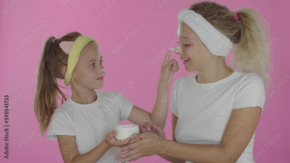 Mother and daughter doing a clay mask for the face family skin care on an isolated red background Mother and daughter doing a clay mask for the face family skin care on an isolated red background