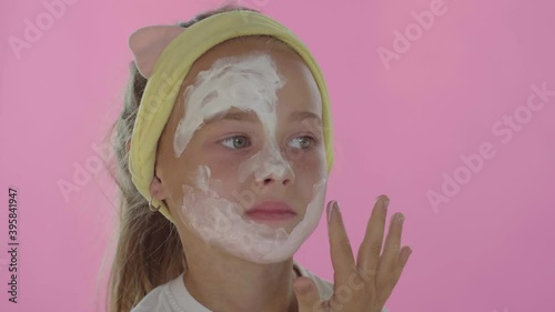 A little girl puts on a cosmetic mask on an isolated red background. Posing for the camera.