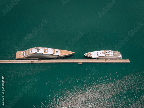 Top view of the luxurious white yachts moored at the long thin quay, blue sea in a sunny day; millionaire concept.