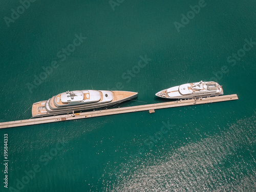 Top view of the luxurious white yachts moored at the long thin quay, blue sea in a sunny day; millionaire concept.