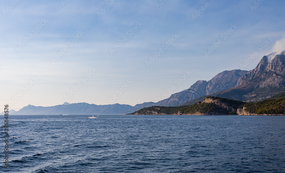 Blick vom Meer auf die Küste in Kroatien. Berge mit Rauchwolken am Himmel. Panorama