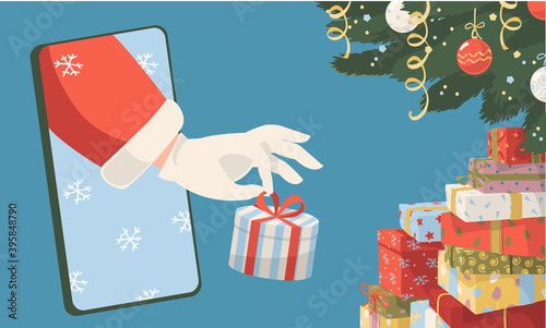 Christmas and New Year online shopping e-commerce and delivery or winter holiday sale concept. Santa's hand from mobile phone  put Christmas gift box under Christmas tree 