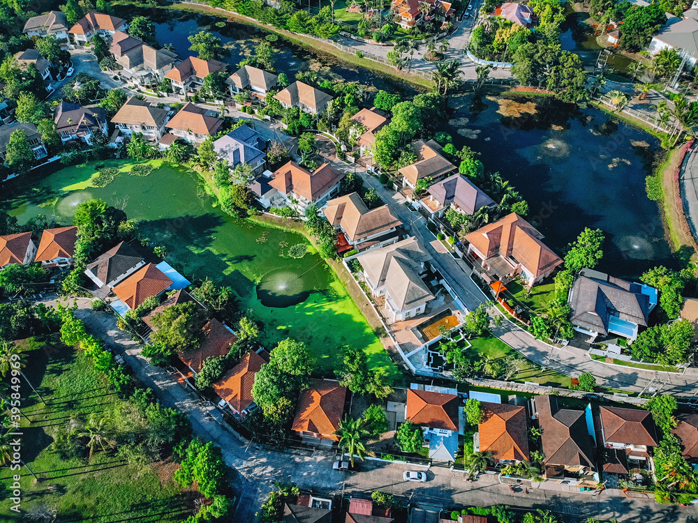 Obraz premium Top view of a line of neighborhood family houses with orange roofs, on both sides surrounded by a swamp and a lake