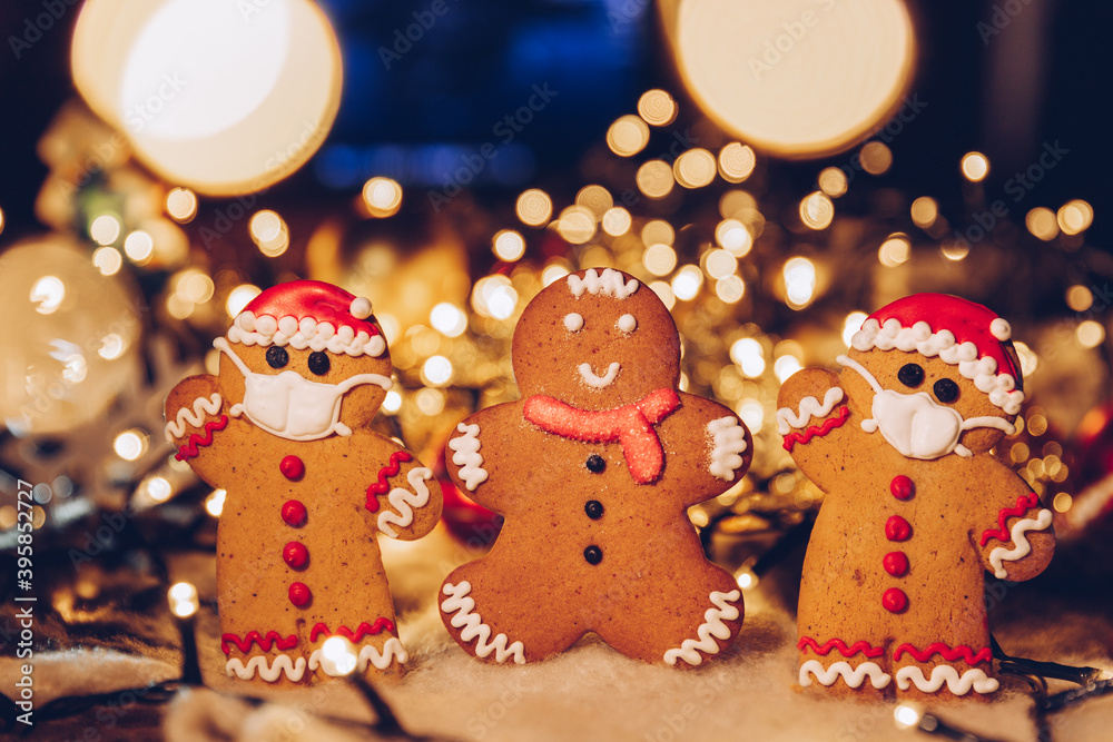 Festive Christmas background with gingerbread men wearing a medical protective mask on their faces. The concept of celebrating the New Year 2021 at home during a coronavirus pandemic. Copy space Festive Christmas background with gingerbread men wearing a medical protective mask on their faces. The concept of celebrating the New Year 2021 at home during a coronavirus pandemic. Copy space