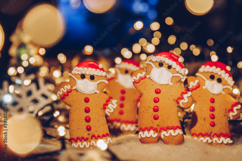 Festive Christmas background with gingerbread men wearing a medical protective mask on their faces. The concept of celebrating the New Year 2021 at home during a coronavirus pandemic. Copy space