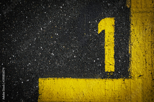 Grey asphalt road, yellow painted number one on grey street, yellow lines like a corner on the road, space for text 