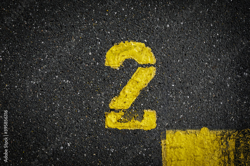Grey asphalt road, yellow painted number two on grey street, yellow lines like a corner on the road, space for text 