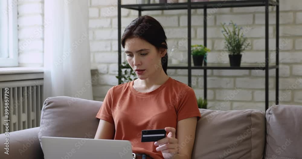 Anxious young caucasian woman holding banking credit card, looking at computer screen, having problems with money transfer or financial transaction, unhappy with system problem, online payment failure