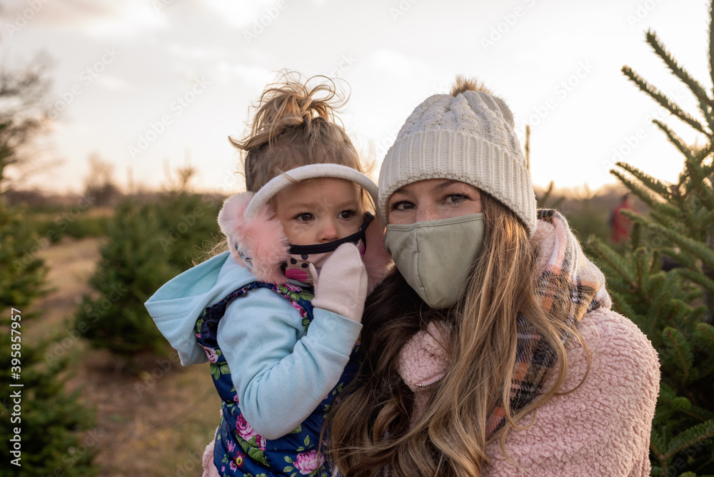 Young mom and toddler girl wearing cloth face masks at the tree farm Young mom and toddler girl wearing cloth face masks at the tree farm