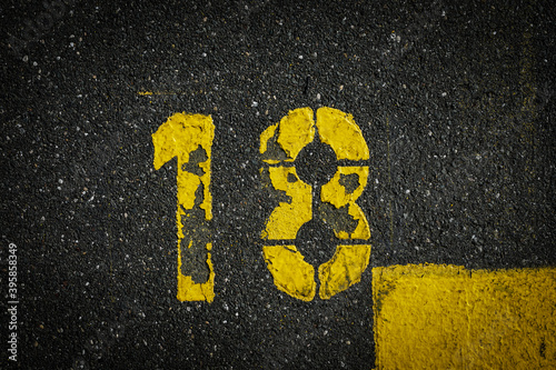 Grey asphalt road, yellow painted number eighteen on grey street, yellow lines like a corner on the road, space for text 