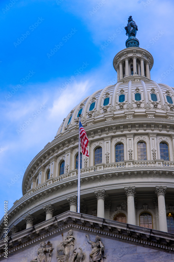 View of American flag on top of entrance to United States Capitol building with marble dome in background with blue sky