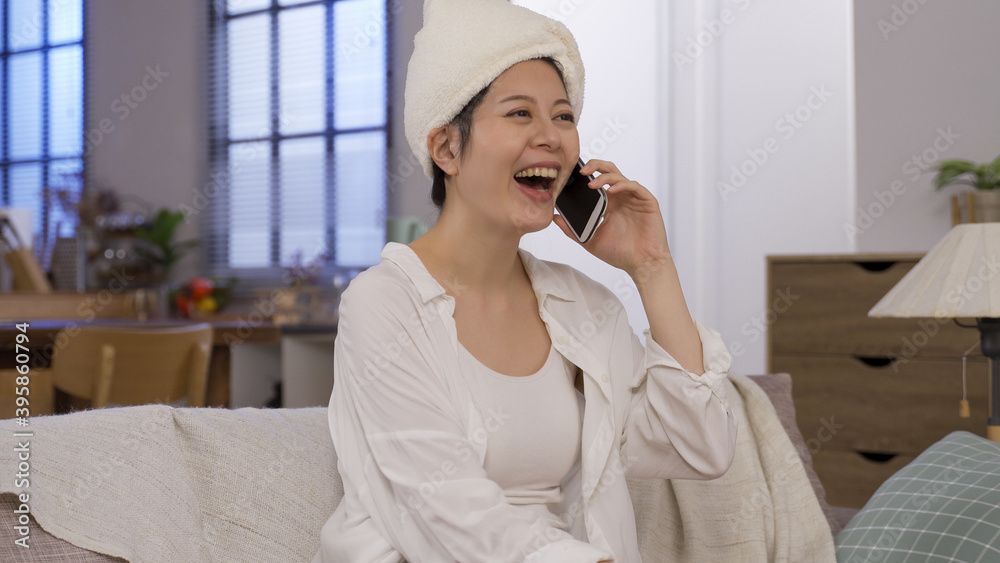 chinese lady holding smartphone is bursting into loud hearty laughter at her friend’s joke after shower with towels on head. chinese lady holding smartphone is bursting into loud hearty laughter at her friend’s joke after shower with towels on head.