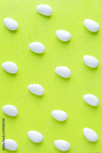 White glazed almond italian candies for bonbonnieres repeating pattern photo on light green background.