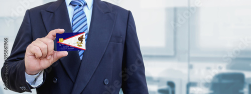 Cropped image of businessman holding plastic credit card with printed flag of American Samoa. Background blurred.