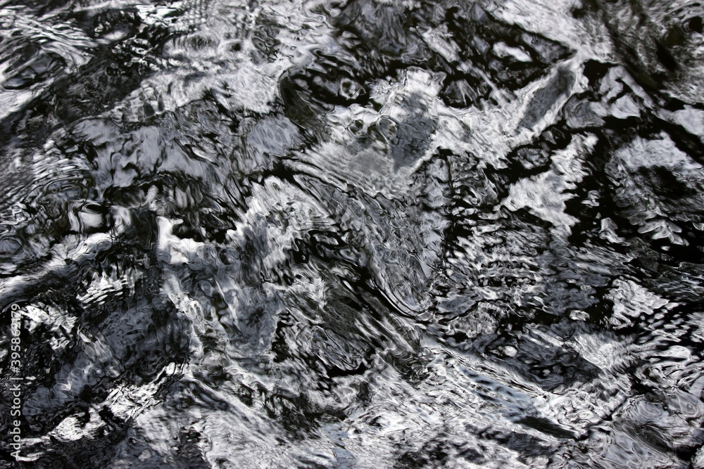 Abstract photography: Monochrome water background in black, white and silver from movement and light reflections on the surface giving a shiny metallic looking effect Abstract photography: Monochrome water background in black, white and silver from movement and light reflections on the surface giving a shiny metallic looking effect