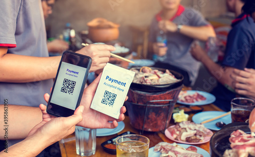 Hand holding smartphone to scan Qr code payment tag with blurry grilled pork and meat on the stove  Thai food buffet payment tag. QR code payment concept to many friends at a party in a  restaurant.