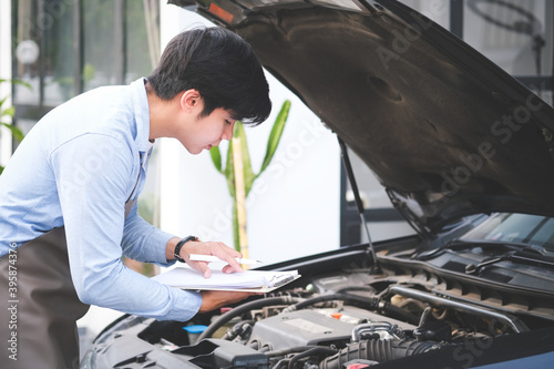 Happy auto repairman writing notes while checklist for repair machine a car in auto repair shop.