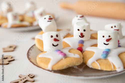Plätzchen mit Marshmallows, Zuckerguss und Schokolinsen die aussehen wie geschmolzene Schneemänner auf Tellern zur Weihnachtszeit