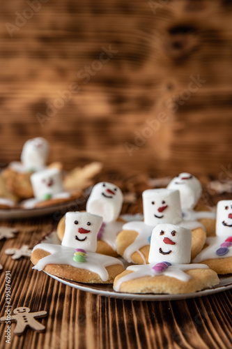 Plätzchen mit Marshmallows, Zuckerguss und Schokolinsen die aussehen wie geschmolzene Schneemänner auf Tellern zur Weihnachtszeit