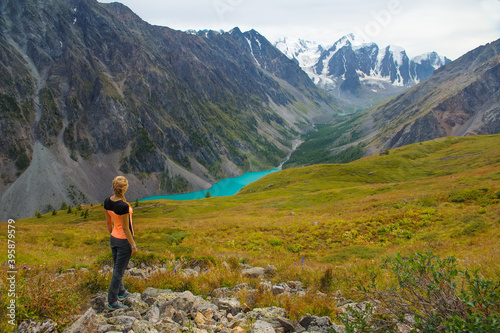 A young girl looks at a mountain lake. The woman admires the beautiful mountains.