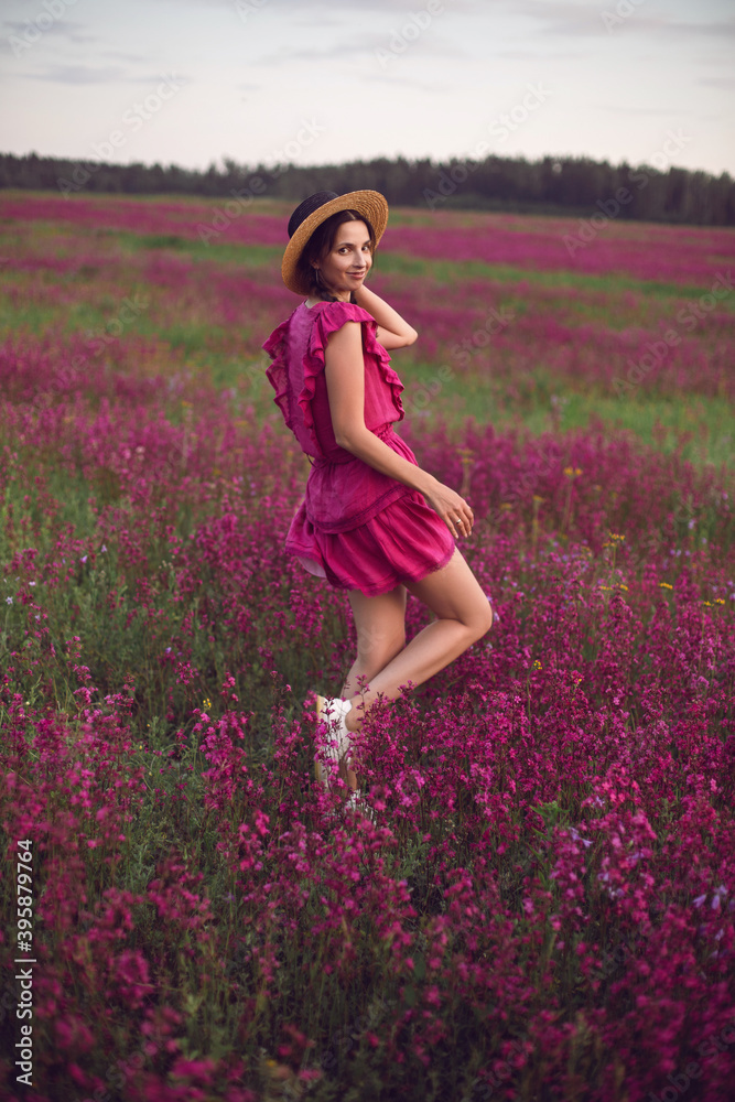 woman in dress and hat stand in a field with pink flowers in nature in summer woman in dress and hat stand in a field with pink flowers in nature in summer