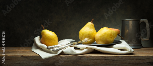 Three pears on old wooden table in vintage setting with cutlery, plate and pewter mug, space for text.