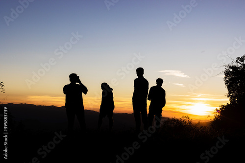 Group of four friends stands on mountain top and looks at sunset.