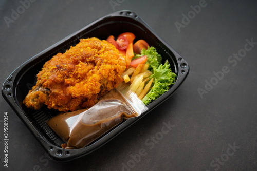 Chicken Chop and fries with  Black Pepper sauce and vegetables. in a take away container.