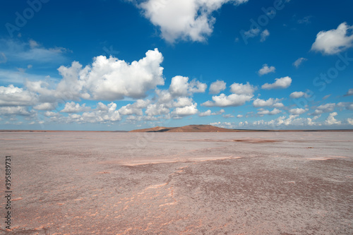 Landscape of a dried up pink salt lake with white clouds in a blue sky