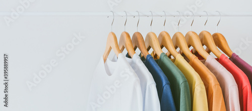 close up collection of colorful t-shirts hanging on wooden clothes hanger in closet or clothing rack over white background, copy space photo